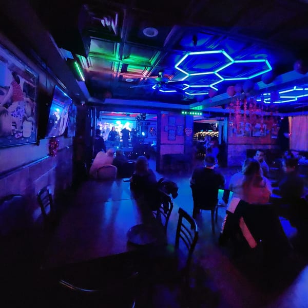 Diners seated in a dark restaurant with blue and green neon lighting, a band performing in the background.