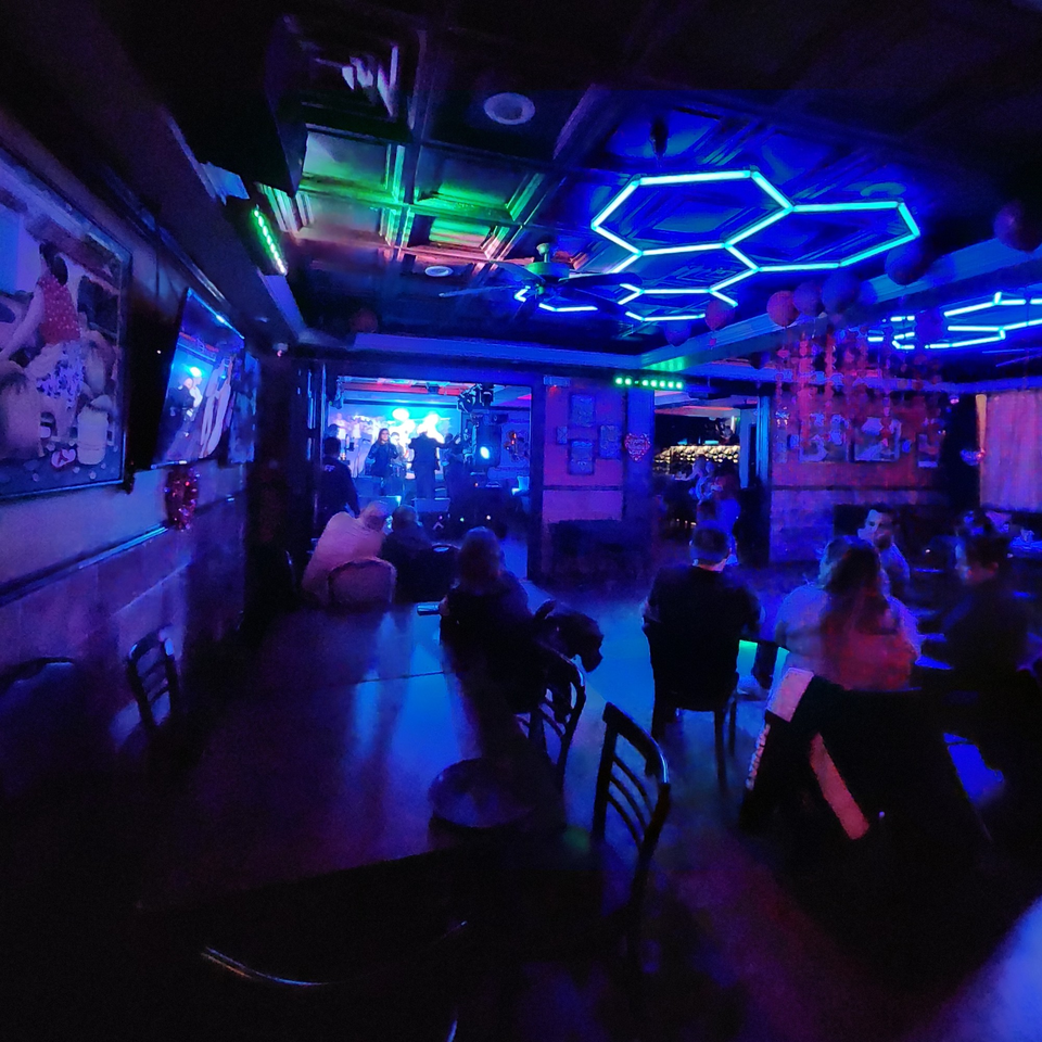 Diners seated in a dark restaurant with blue and green neon lighting, a band performing in the background.