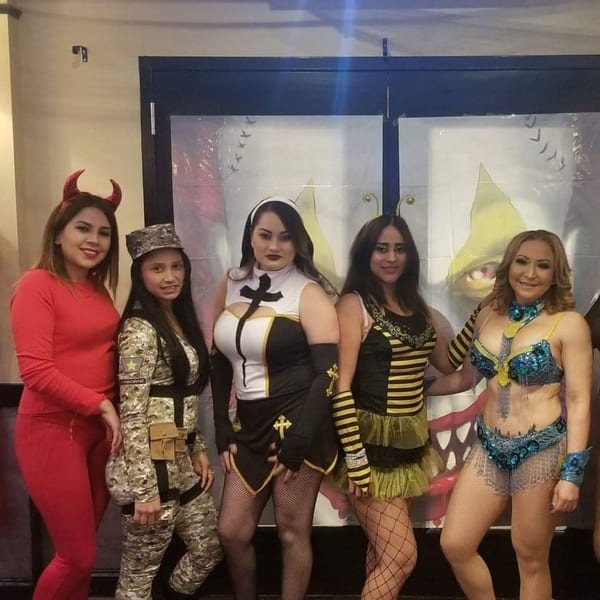 Five women in various Halloween costumes, including a devil, soldier, nun, bee, and belly dancer.