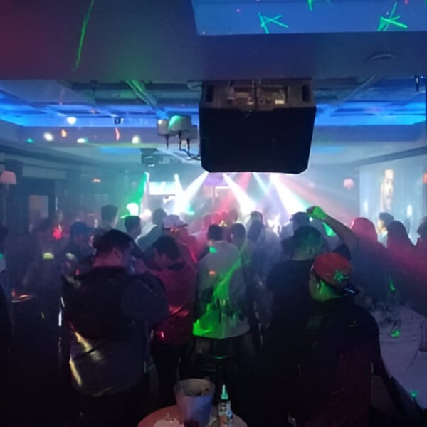 A lively nightclub scene with a crowd of people dancing under colorful laser lights.