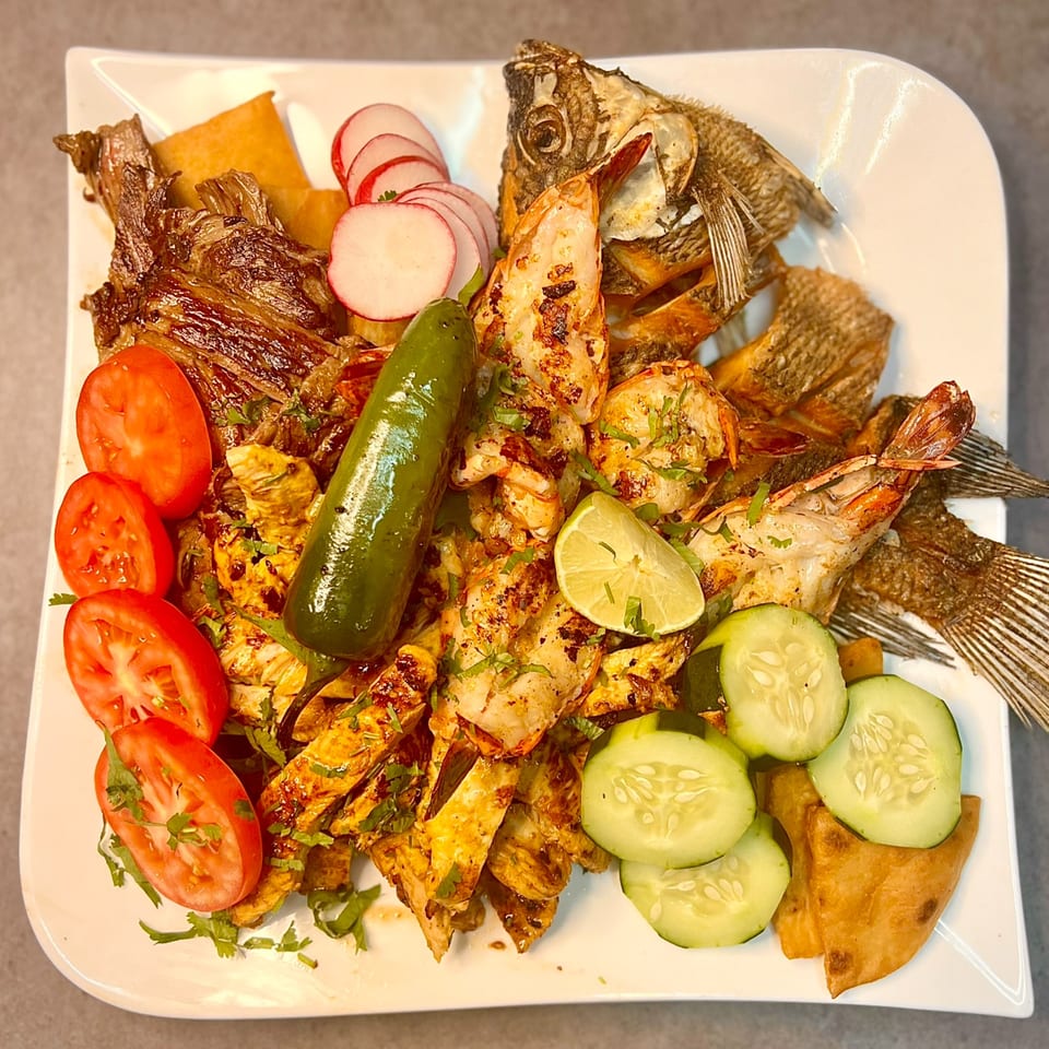 A large platter of grilled shrimp, fried fish, chicken, tomatoes, radishes, cucumbers, and a green pepper.