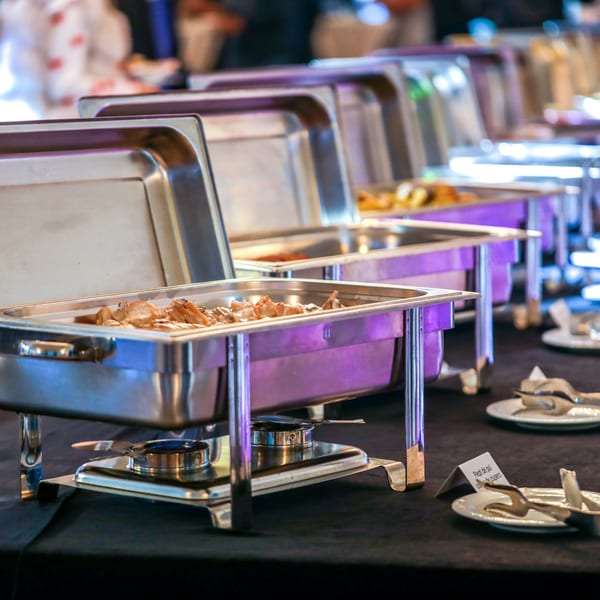 A buffet line of several stainless steel chafing dishes filled with Salvadoran food on a black tablecloth.