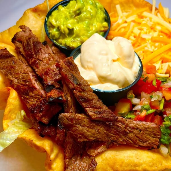 Grilled steak strips with guacamole, crema, pico de gallo, and shredded cheese in a tortilla bowl.