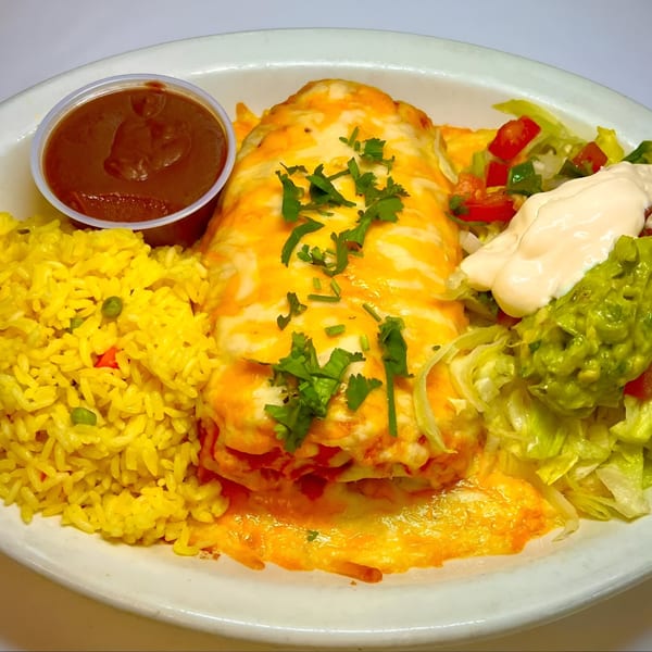 A large Salvadoran burrito covered in melted cheese and cilantro, served with yellow rice, salsa, guacamole, and sour cream.