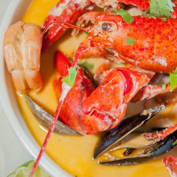 A close-up of a vibrant Salvadoran seafood soup with lobster, shrimp, and mussels in a yellow broth.
