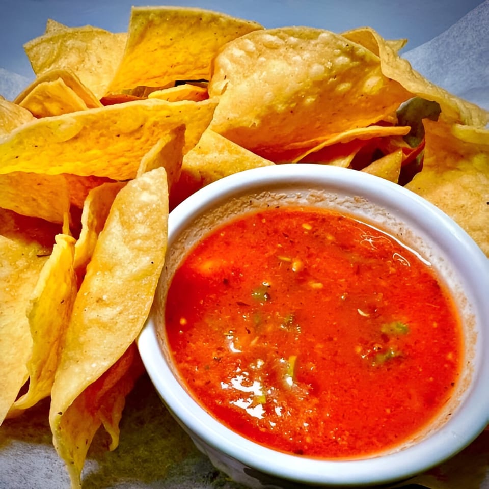A white bowl of vibrant red salsa sits next to a pile of golden tortilla chips.