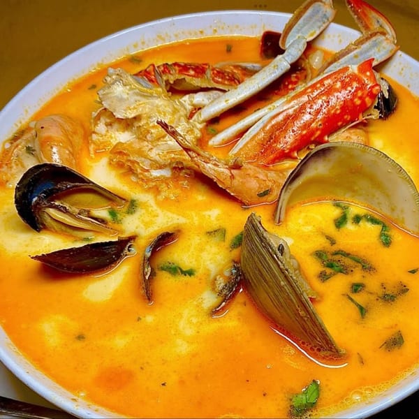 A vibrant orange seafood soup with crab, mussels, and clams in a white bowl.