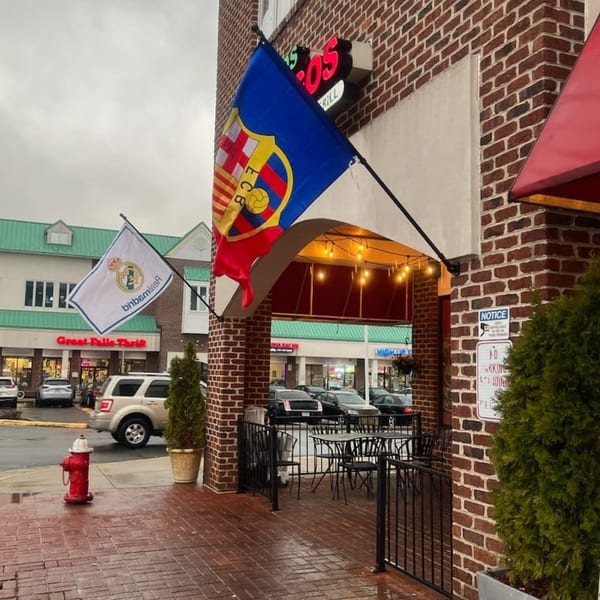 Exterior of Tipicos Los Amigos with outdoor seating, flags, and a brick facade on a cloudy day.