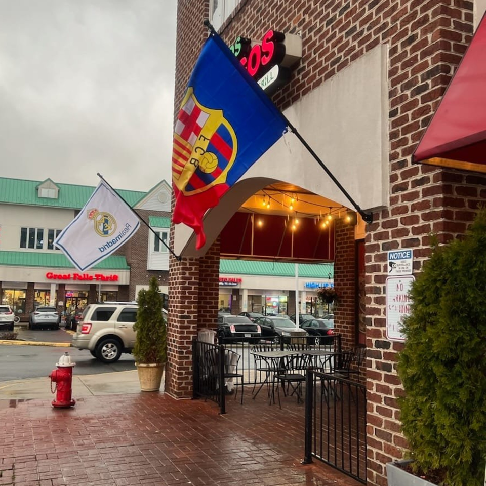 Exterior of Tipicos Los Amigos with outdoor seating, flags, and a brick facade on a cloudy day.