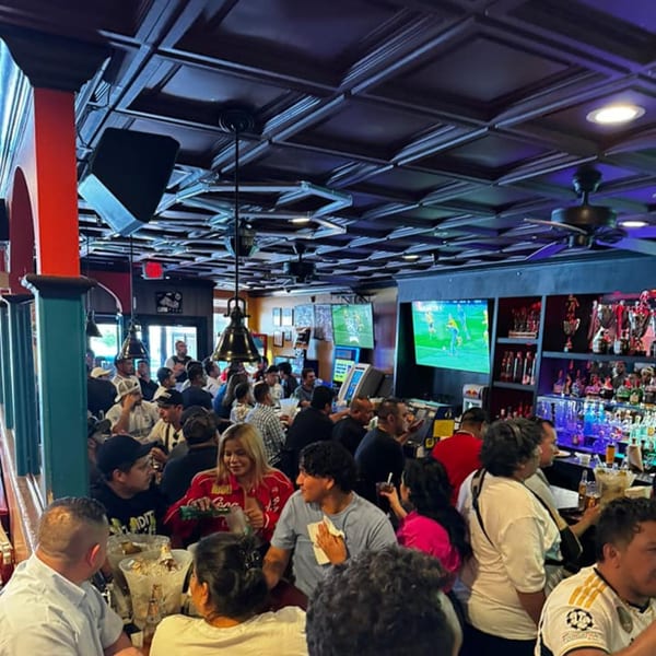 A lively Salvadoran restaurant interior with many patrons, a bar, and televisions showing sports.
