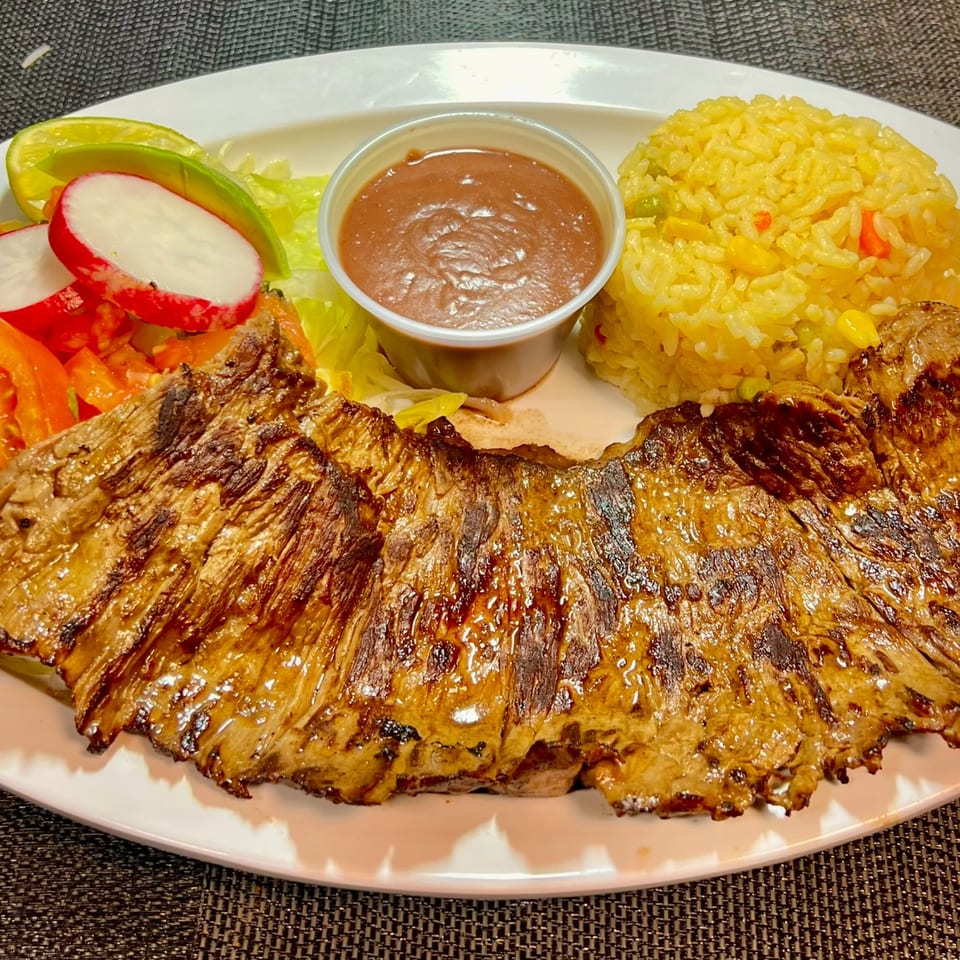 Grilled skirt steak with yellow rice, salad, and a side of brown sauce at Tipicos Los Amigos.